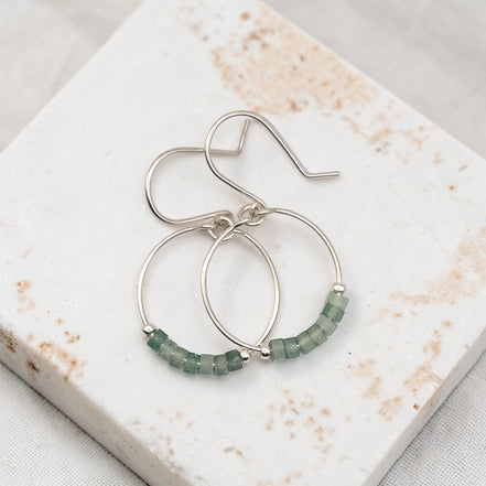 Silver hoop earrings with green aventurine beads on a marble surface