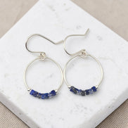 Silver hoop earrings with blue gemstones on a marble surface