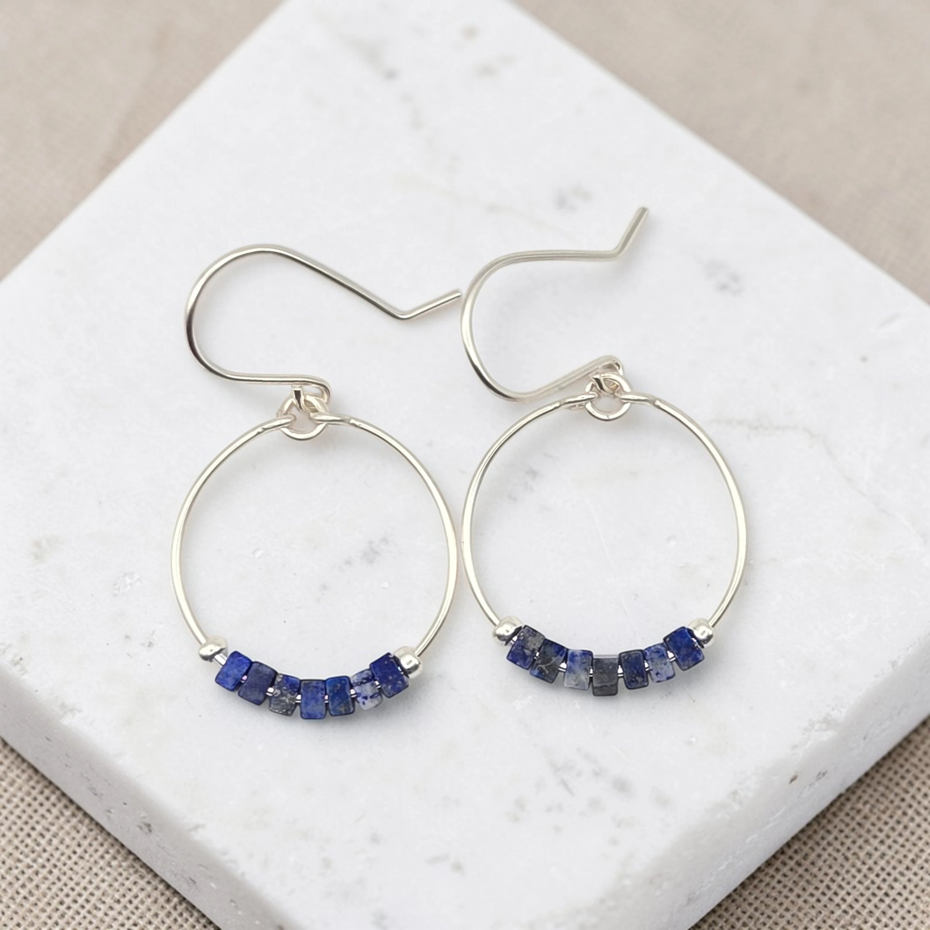 Silver hoop earrings with blue gemstones on a marble surface