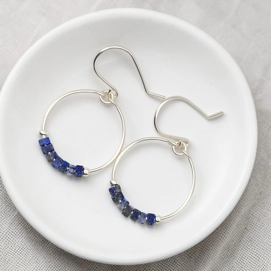 Silver hoop earrings with blue beads on a white plate
