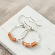 Silver hoop earrings with orange beads on a white marble surface.