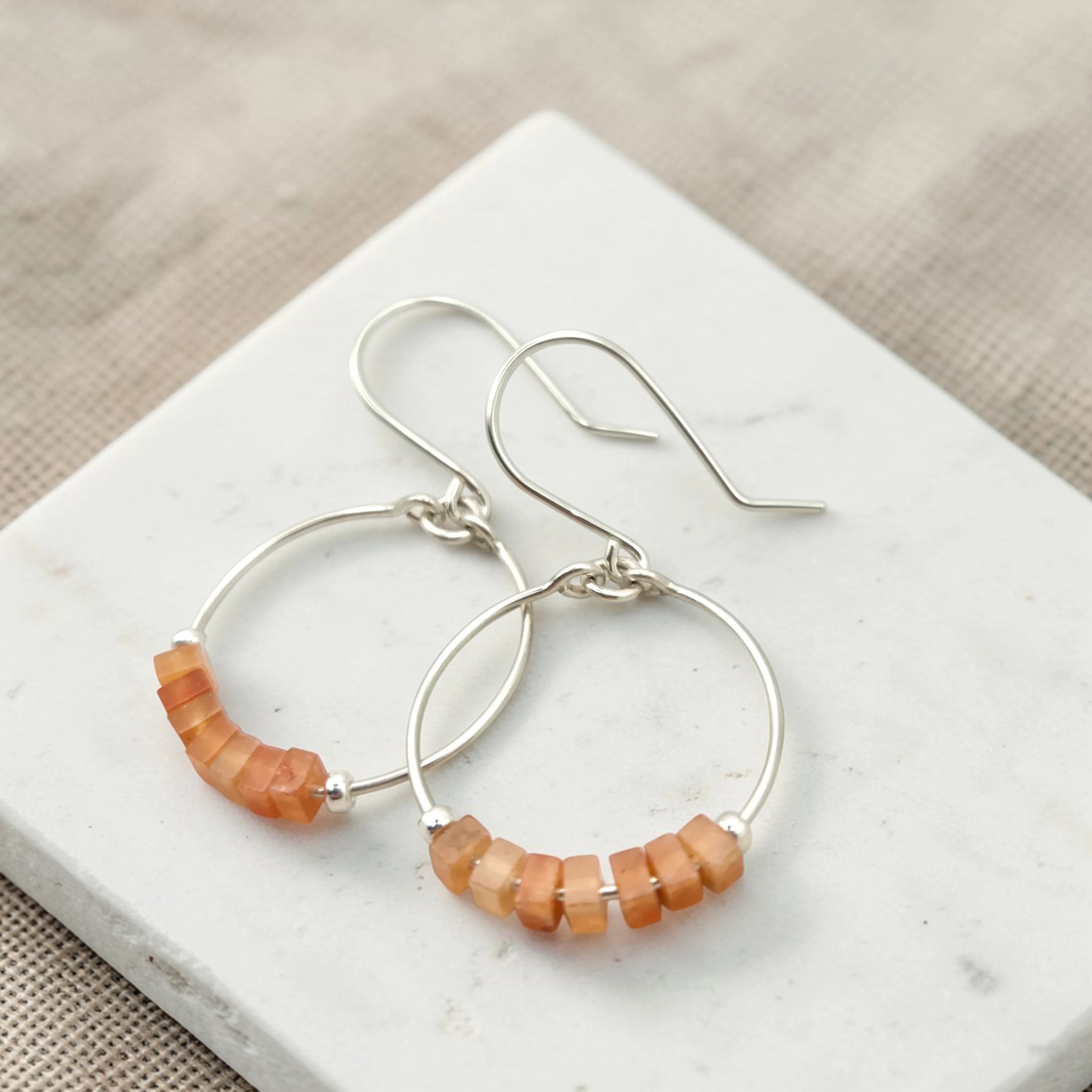 Silver hoop earrings with orange beads on a white marble surface.