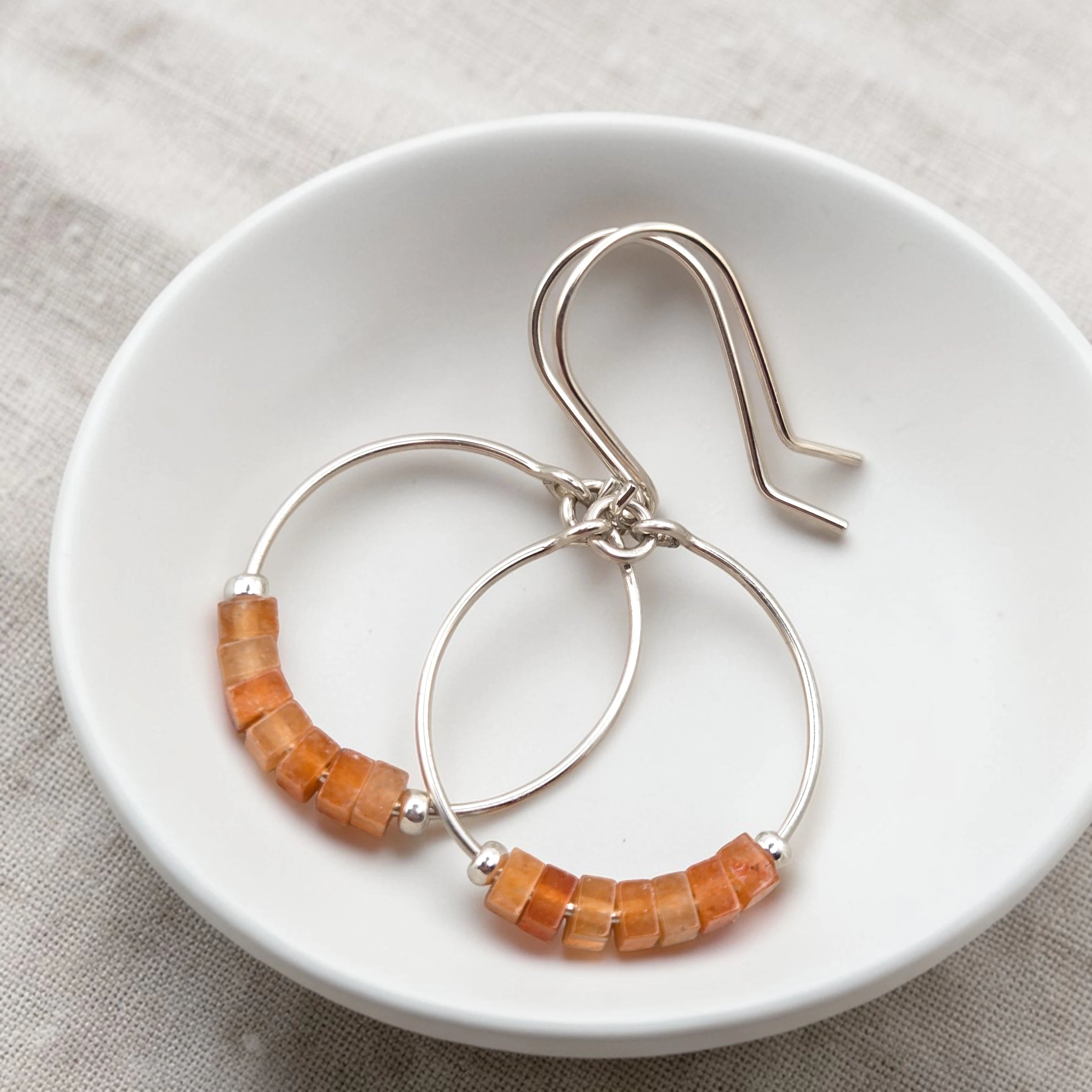 Silver hoop earrings with orange aventurine beads on a white dish.