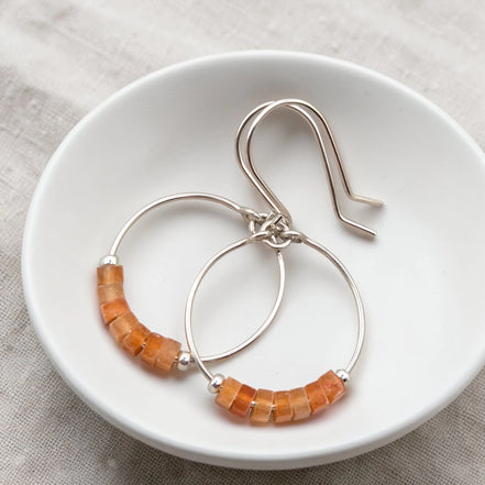Silver hoop earrings with orange aventurine beads on a white dish.