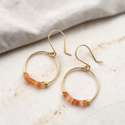 Gold hoop earrings with orange beads on a marble surface
