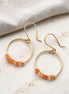 Gold hoop earrings with orange beads on a marble surface