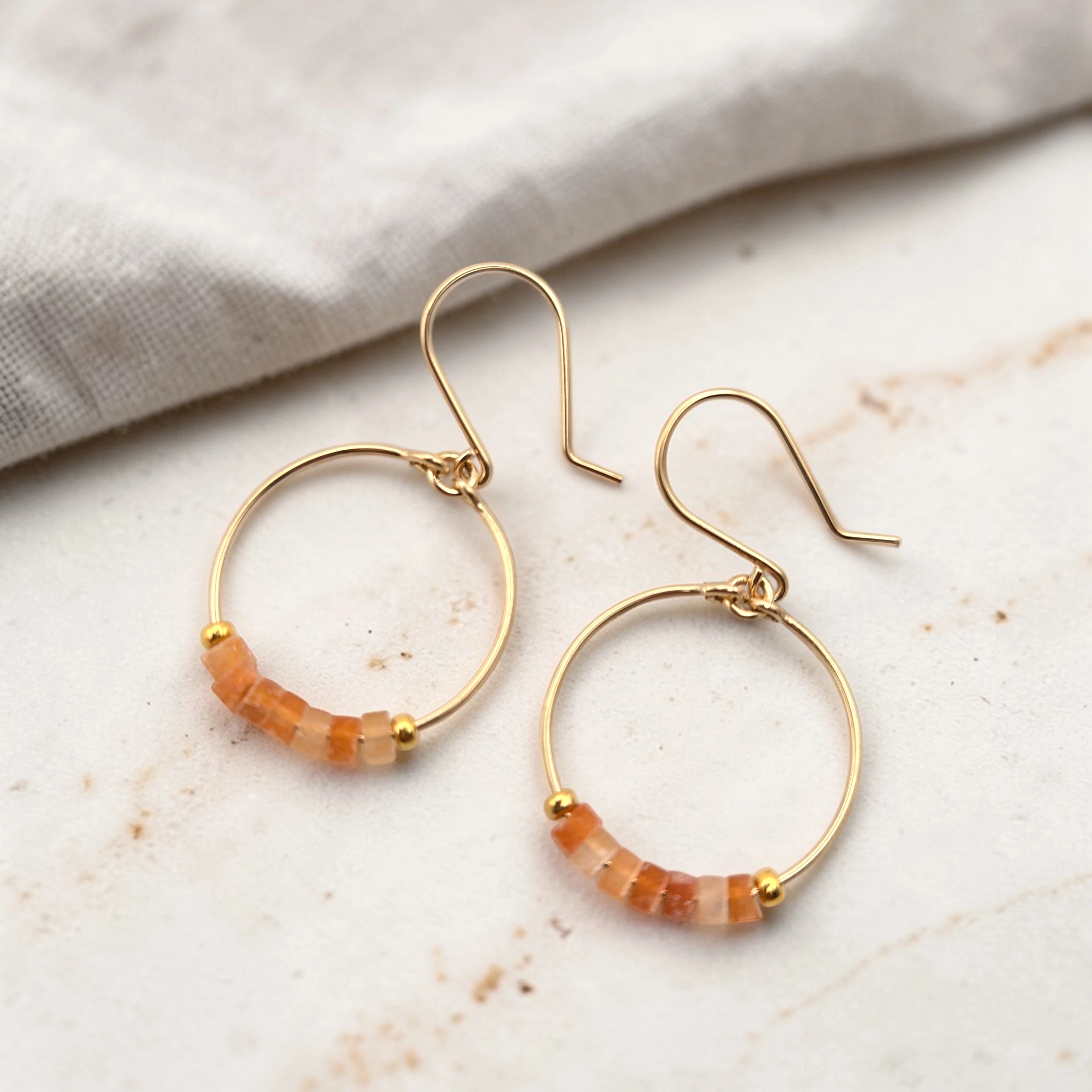 Gold hoop earrings with orange beads on a marble surface