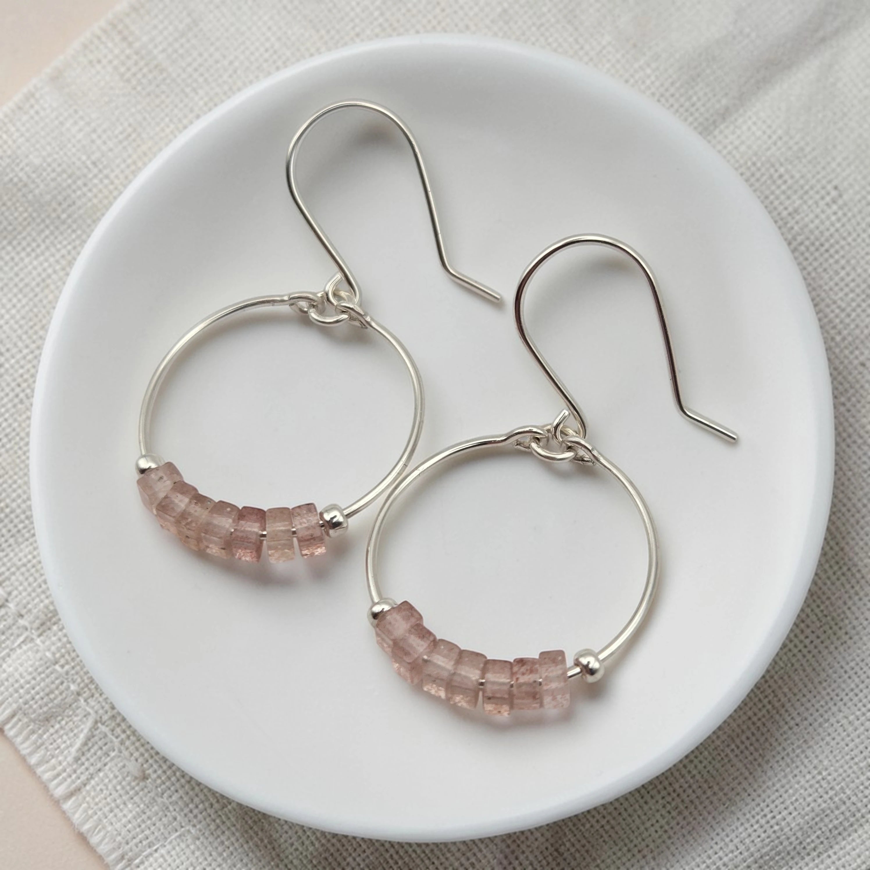 Silver hoop earrings with pink beads on a white plate