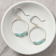 Silver hoop earrings with amazonite beads on a white dish.