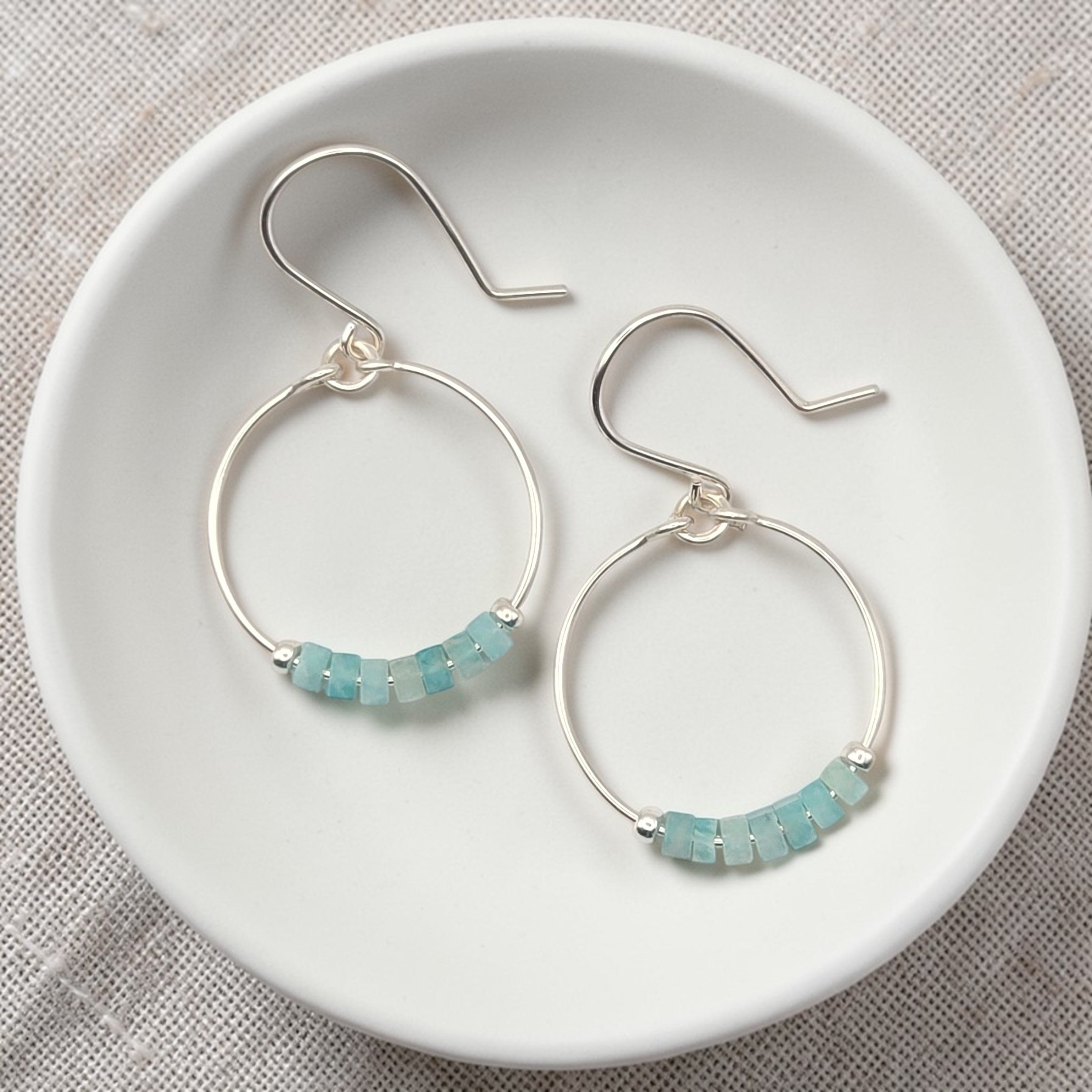 Silver hoop earrings with amazonite beads on a white dish.