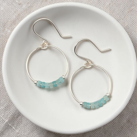 Silver hoop earrings with amazonite beads on a white dish.