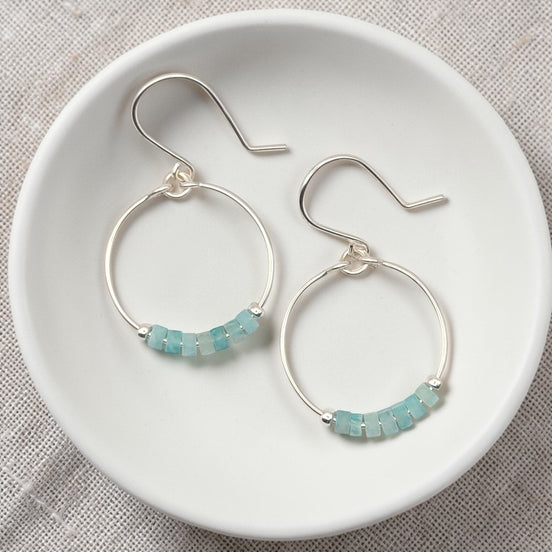Silver hoop earrings with amazonite beads on a white dish.