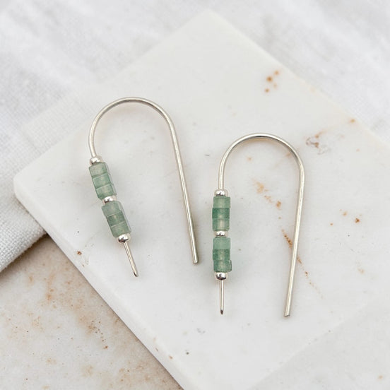 Pair of earrings with green beads on a marble surface