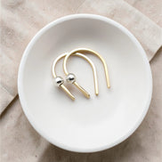 tiny handmade gold huggie earrings with a silver bead laying in a white porcelain bowl