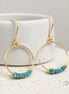 Gold hoop earrings with turquoise beads on a white surface.