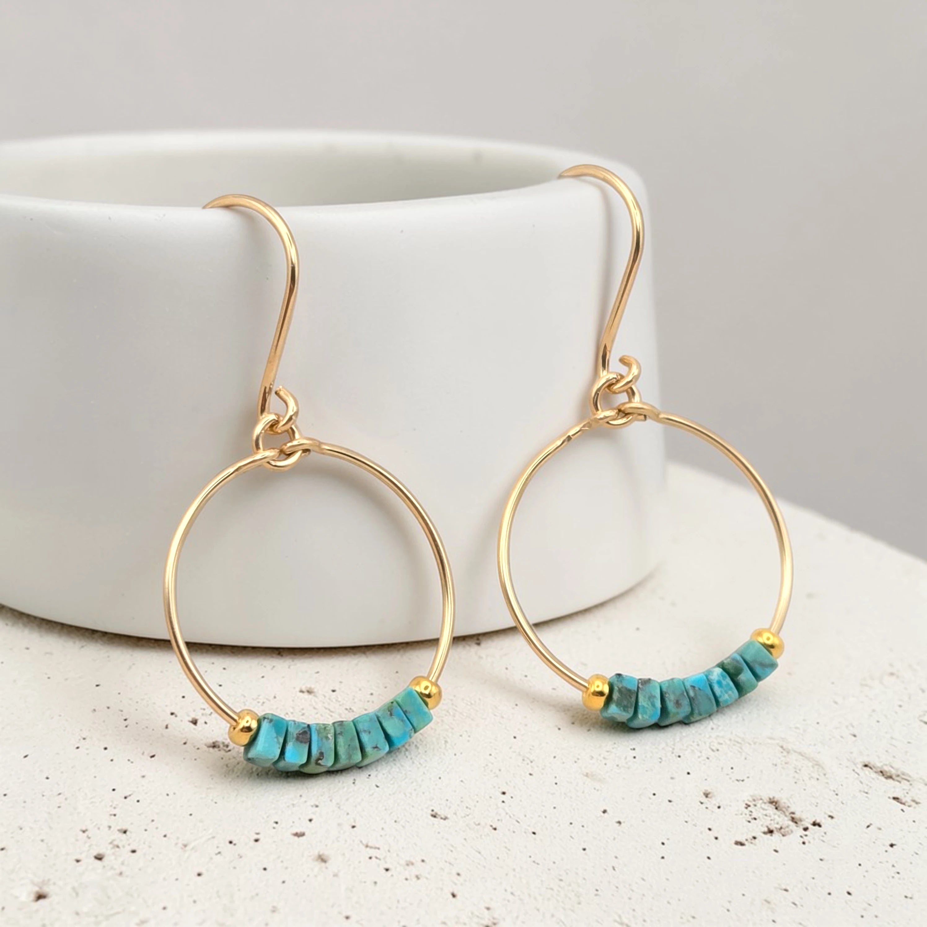 Gold hoop earrings with turquoise beads on a white surface.