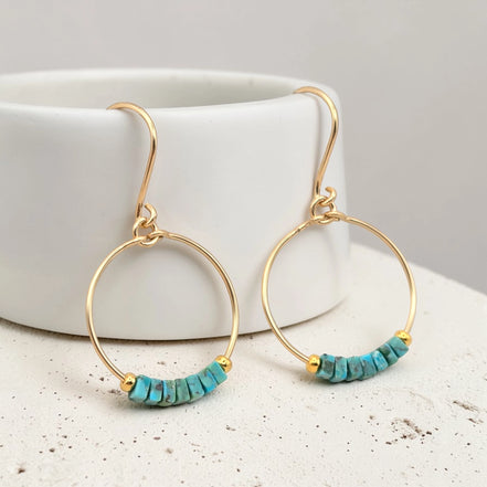 Gold hoop earrings with turquoise beads on a white surface.