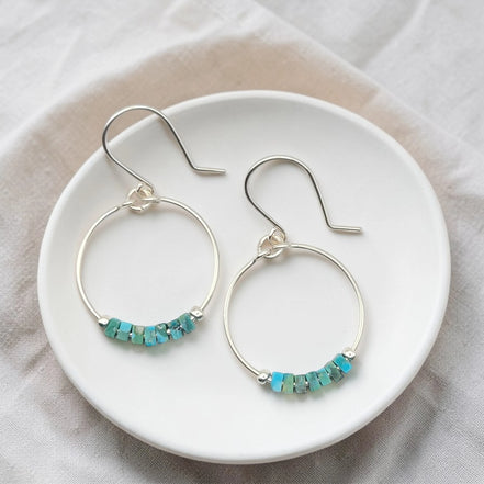 Silver hoop earrings with turquoise beads on a white plate.