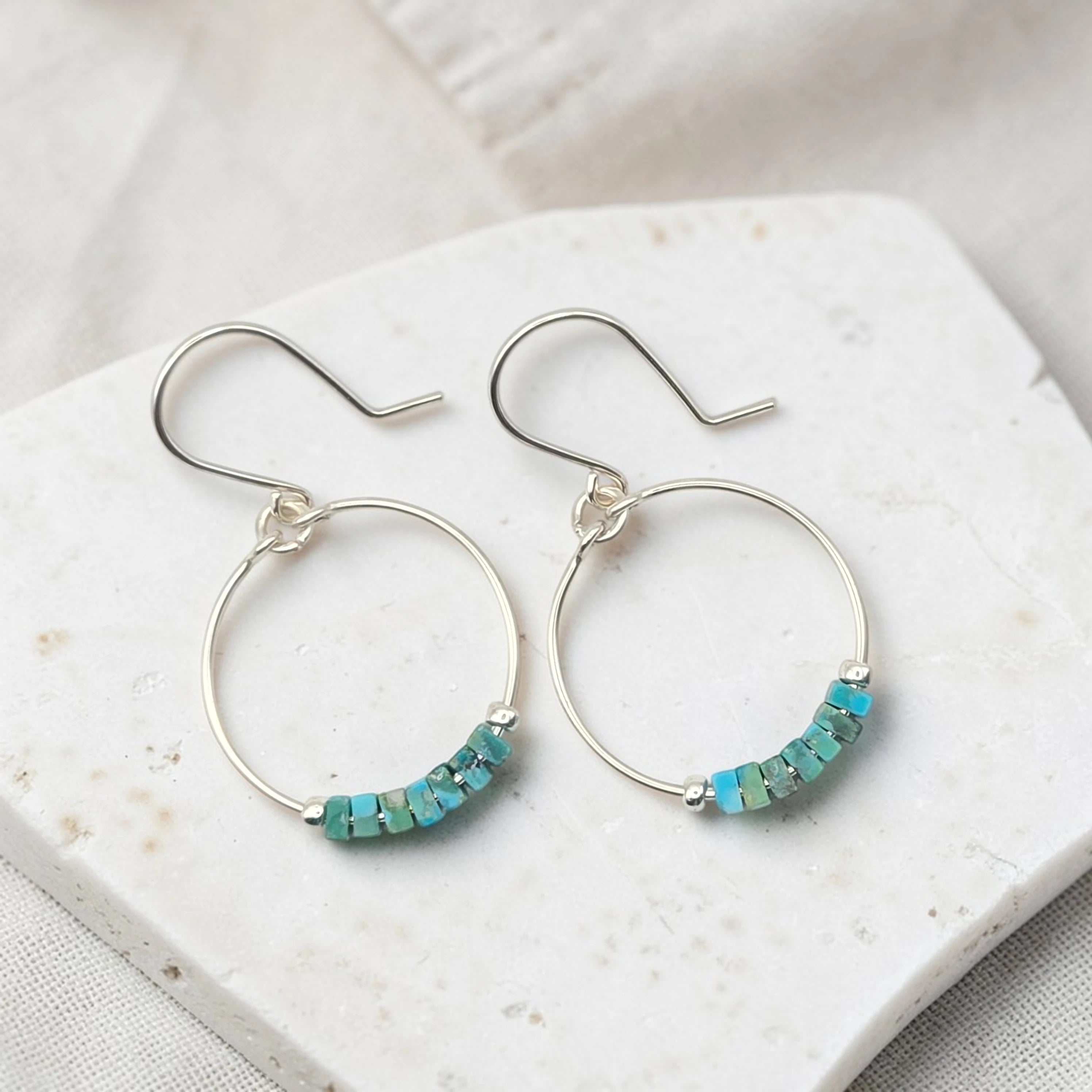 Silver hoop earrings with turquoise beads on a white stone surface