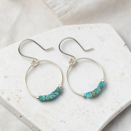 Silver hoop earrings with turquoise beads on a white stone surface