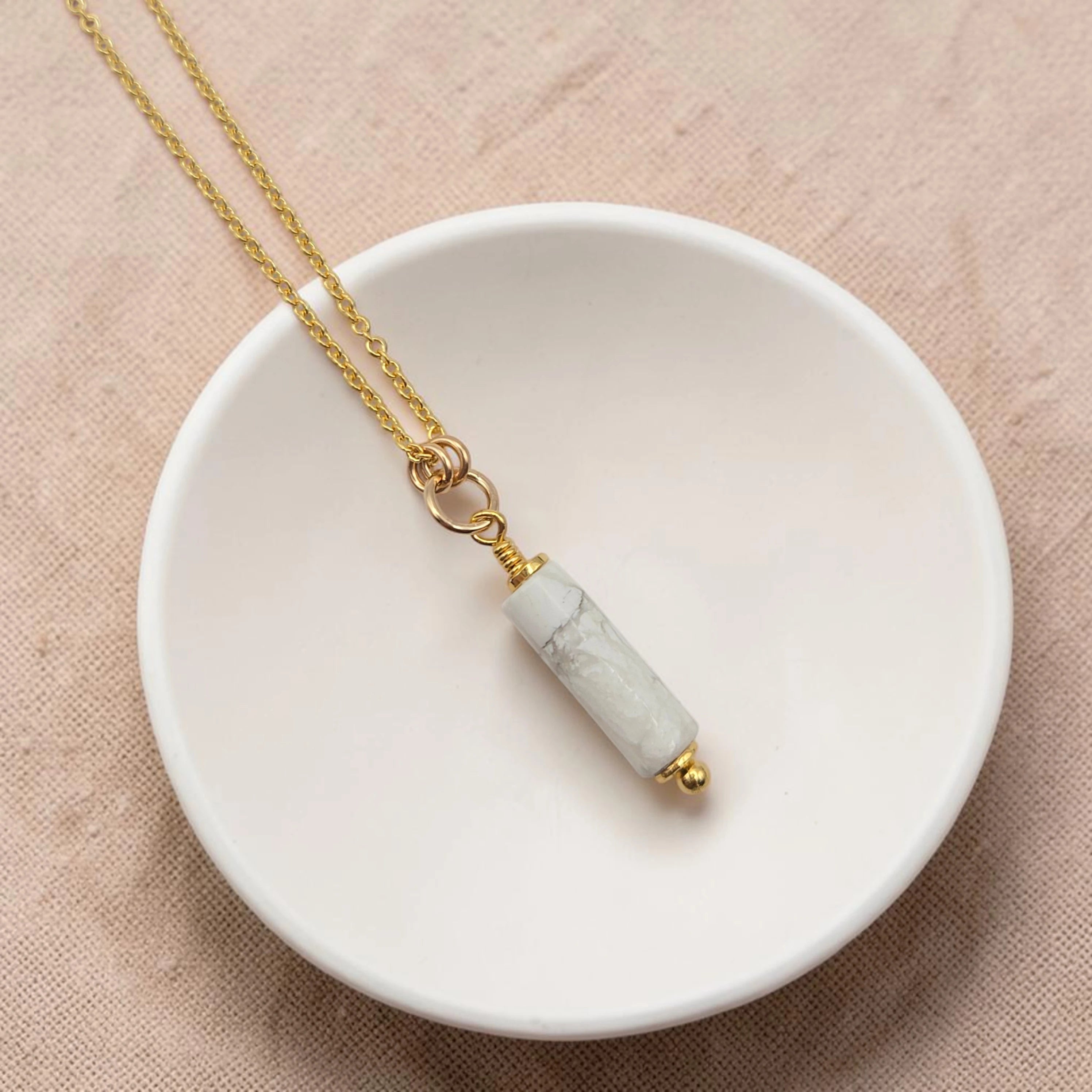 Necklace with a cylindrical pendant on a white dish against a beige background