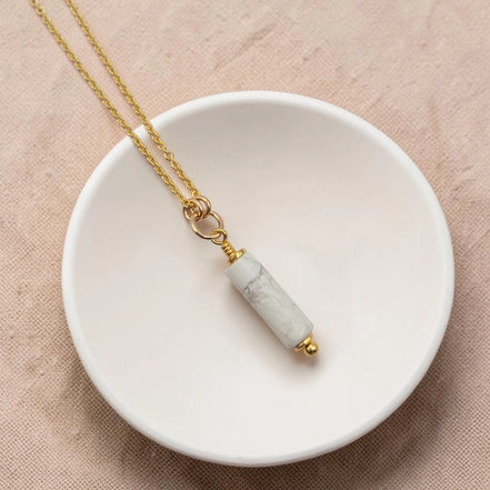 Necklace with a cylindrical pendant on a white dish against a beige background