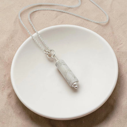 Necklace with a marble-textured pendant on a white dish against a beige background
