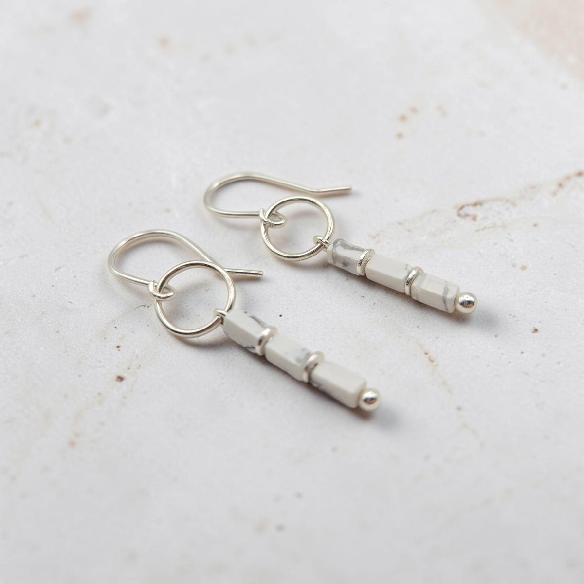 A pair of silver dangle earrings with faceted white beads and small silver ball accents, displayed on a light textured surface.