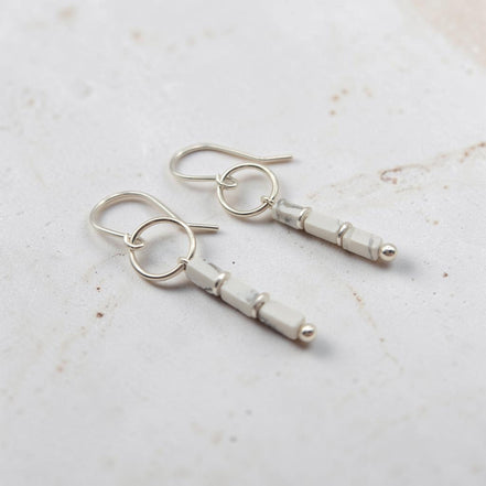 A pair of silver dangle earrings with faceted white beads and small silver ball accents, displayed on a light textured surface.