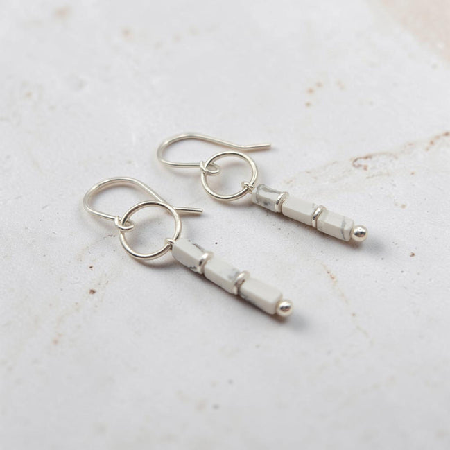 A pair of silver dangle earrings with faceted white beads and small silver ball accents, displayed on a light textured surface.