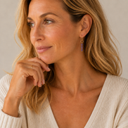 A close-up of a woman wearing a delicate gold hoop earring with a vertical drop of small amethyst beads, paired with a cream knit sweater.
